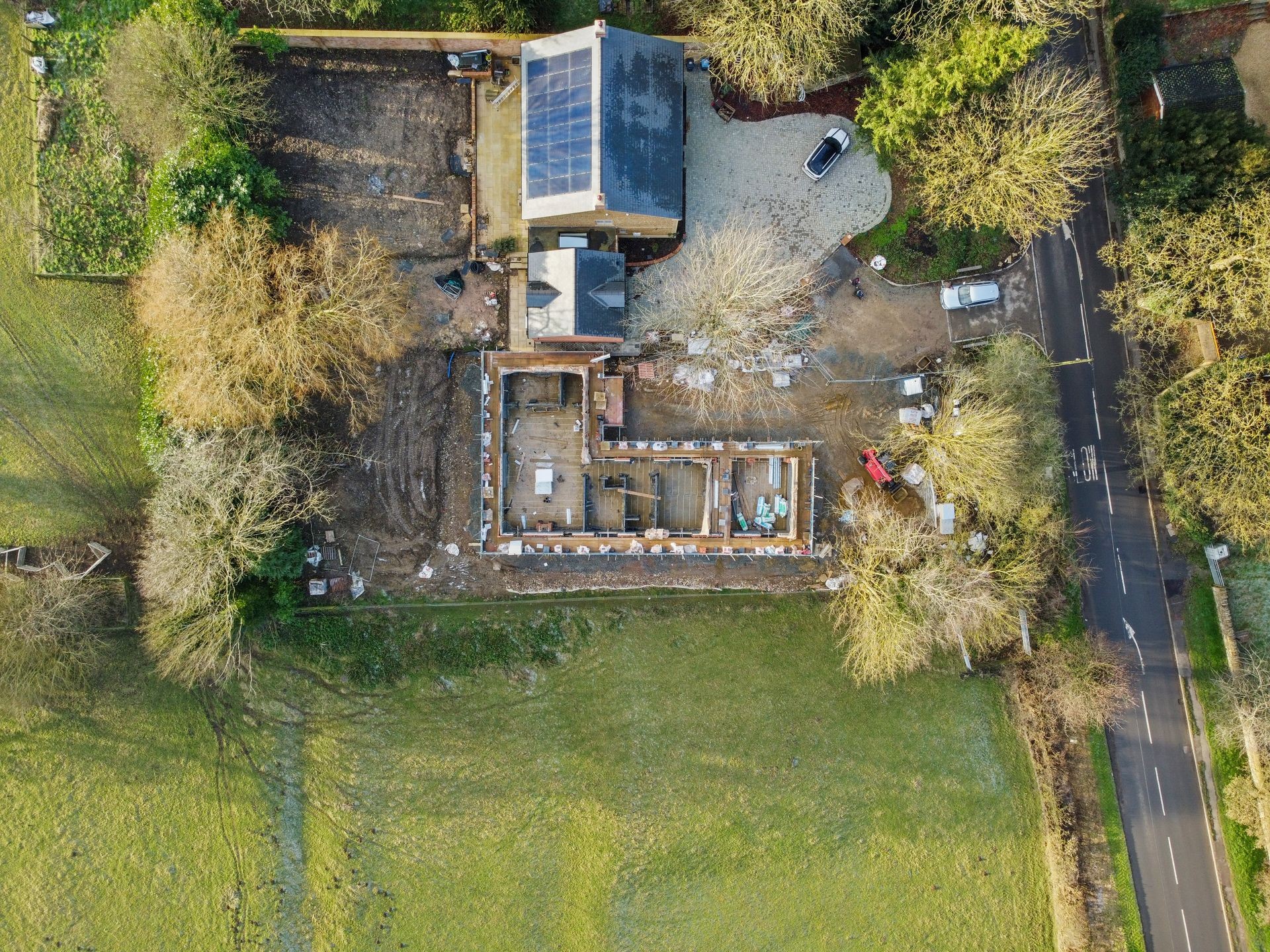 Aerial view of a construction site with a partially built house, surrounded by trees and roads.