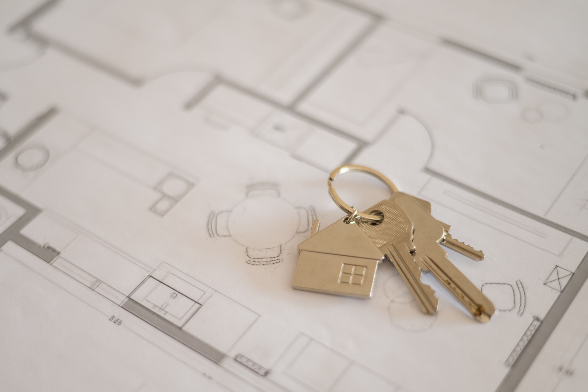 House keys with house-shaped keychain are lying on top of architectural plans, symbolizing the exciting process of buying, selling, or renting a property and securing a mortgage for a new home